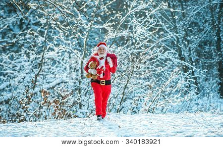 Santa Claus Going With A Bag Of Gifts In The Winter On Snow-covered Field. Santa Claus Coming To The