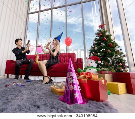 Young asian adult couple celebrating New year and Christmas holiday together with Firecrackers and confetti in living room of big apratment with christmas tree decoration.