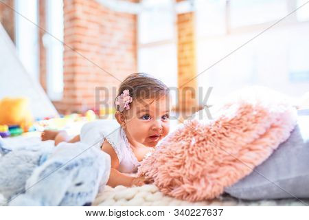 Beautiful infant happy at kindergarten around colorful toys lying on blacket