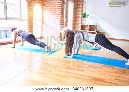 Young beautiful group of sportswomen smiling happy practicing yoga doing plank pose at gym