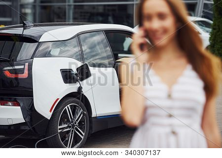 Image Focus Technique. With Phone. Woman On The Electric Cars Charge Station At Daytime. Brand New V