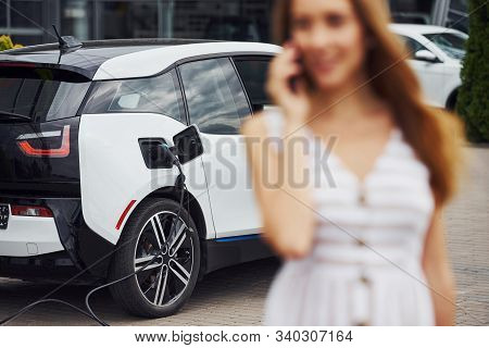 Image Focus Technique. With Phone. Woman On The Electric Cars Charge Station At Daytime. Brand New V