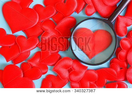 A Lot Of Red Hearts On A Blue Background. One Of Them Is Examined Under A Magnifying Glass. The Choi