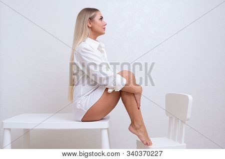 Beautiful Dreaming Female In A White Shirt Sits On A Bench With Bare Legs. The Concept Of Skin Care,