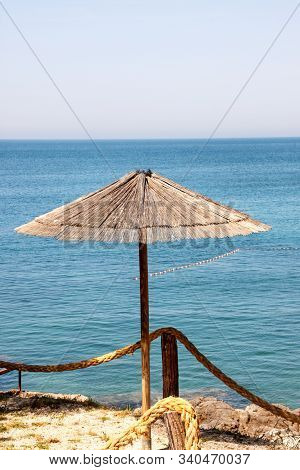 Lonely Wicker Sun Umbrella At Mediterranean Beach By Sea. Natural Bamboo Sunshades And Summer Umbrel