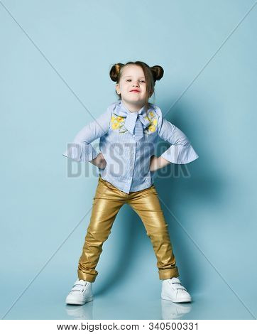 Playful Frolic Impish Kid Girl With Funny Buns And In Blue Shirt And Gold Leather Pants Is Cool Posi