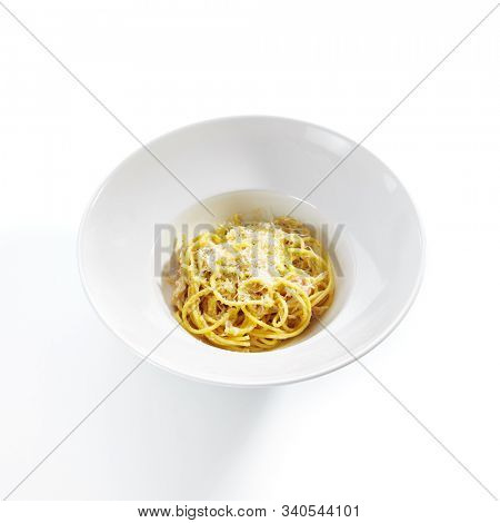 Italian spaghetti alla carbonara with grated parmesan, hard pecorino romano cheese, fried bacon, guanciale or pancetta, egg sause and black pepper on white restaurant plate isolated side view