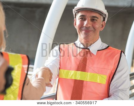 A Man With A European Engineer Wearing A Uniform And White Hat Holding Hands With A Customer A Busin