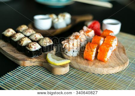 A Set Of California Rolls,some Cream Cheese, Shrimp On Wooden Platters And The Black Table. With Gin