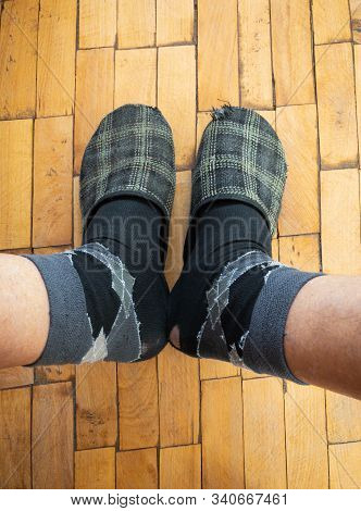 Top View On Male Legs Wearing Old Worm Socks And Slippers Standing On Old Parquetry