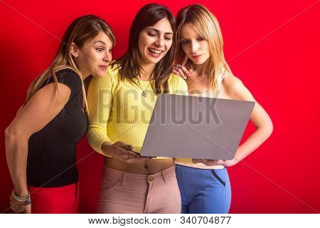 Stock Photo Of Three Girls Standing With A Laptop On A Red Background