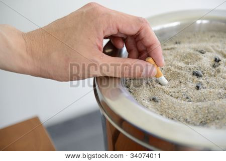 มือชาย Stubbing ออกบุหรี่ในช่องเขี่ยทราย
