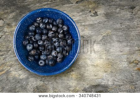 A blue enamelware bowl filled with fresh ripe blueberries on a slate table top, with copy space.