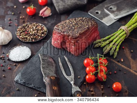 Slice Of Raw Beef Topside Joint With Salt And Pepper On Stone Chopping Board With Fork And Knife, Ga