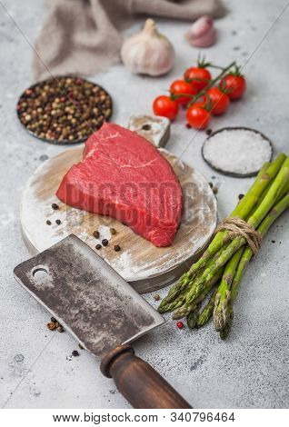 Slice Of Raw Beef Sirlion Steak On Round Chopping Board With Tomatoes,garlic And Asparagus Tips And 