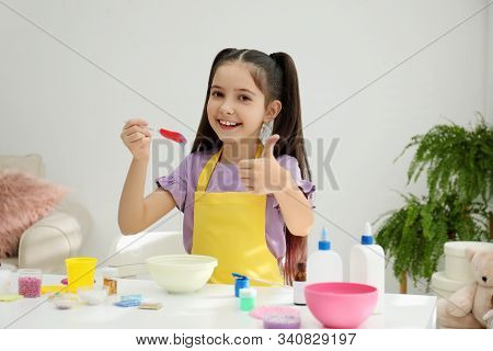 Cute Little Girl Mixing Ingredients With Silicone Spatula At Table In Room. Diy Slime Toy