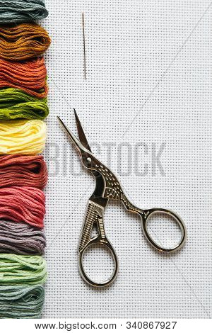 Flat Lay Cross Stitch: Multi-colored Floss Thread, Scissors For Needlework, A Needle On A White Canv