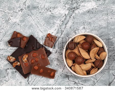 Broken Chocolate Bars, Sweet Cashew, Inshell Macadamia And Almond On Gray Stone Background. Top View