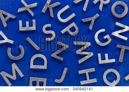 Abstract Flat Background Of Silver Metal English Alphabet Characters On Blue Background.