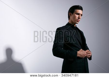Young Man Poses In Studio With Attitudine, Looking At Camera, Adjusting His Suit, Isolated On White 