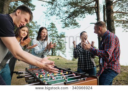 Friends Play Table Football Or Kicker Outdoors. Players And Fans Rejoice In The Victory.