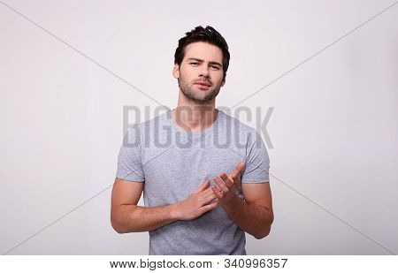 Handsome Young Man In A Gray T-shirt Looking At Camera, Standing On Gray Background. Handsome Young 