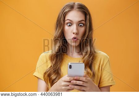 Young Girl Shocked Reading Messages In Friends Smartphone Folding Lips Popping Eyes In Amazement At 