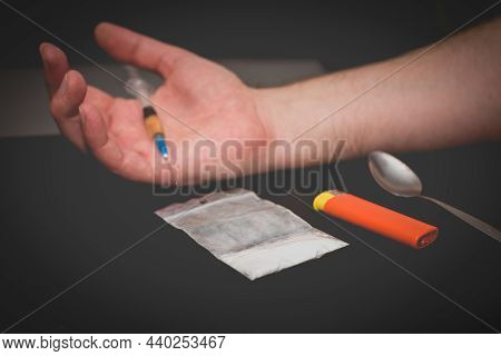 Drug Addict Hand With Syringe On Dark Room With A Bag Of Drugs A Spoon And A Lighter.toned.