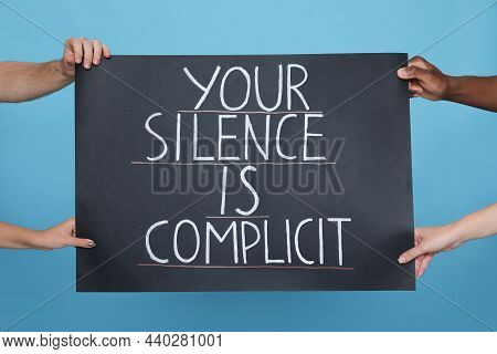 People Holding Sign With Phrase Your Silence Is Complicit On Light Blue Background, Closeup. Racism 