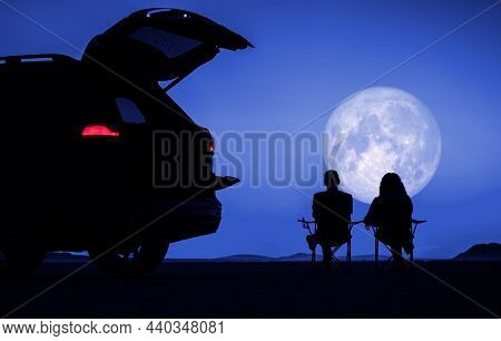 Couple Seating Next To Their Car And Enjoying Full Moon Vista During Scenic Desert Night. Outdoors P