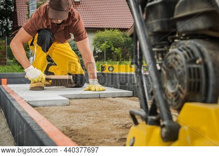 Residential Pathway Concrete Bricks Paving By Caucasian Worker. Compacting Machine In A Front.