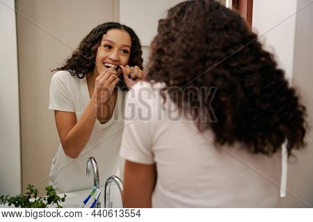 Helathy Multi-cultural Young Female Flossing Her Teeth In Modern Bathroom Mirror.