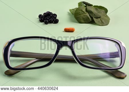Blueberries, Fresh Spinach And A Capsule Of Vitamins For Vision And Glasses For Eyes On A Light Gree