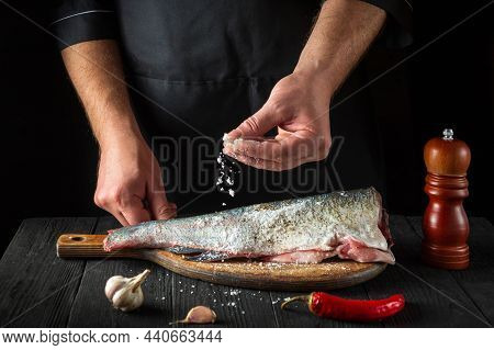 The Chef Prepares Fresh Fish Sprinkling Salt. Preparing To Cook Fish Food. Working Environment In Th