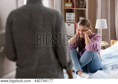 misbehavior, conflict and family concept - mother entering room and sad daughter sitting on bed at home