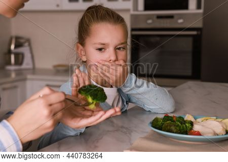 Mother Feeding Her Daughter In Kitchen, Closeup. Little Girl Refusing To Eat Dinner