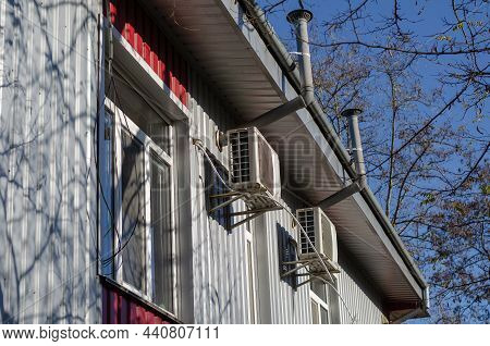 A Gray-red Industrial Building Against A Blue Sky. The Building Is Lined With Metal Profile Sheets. 