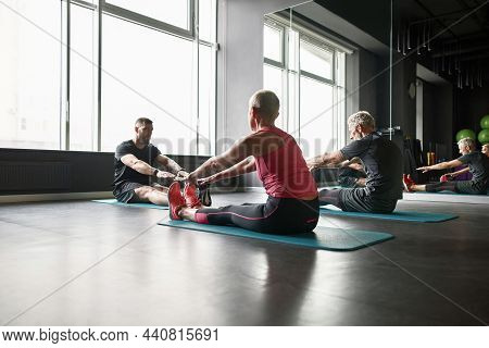 Middle Aged Fit Woman And Elderly Bearded Man Sitting On Mats, Stretching Trying To Rich Tip Toes. P