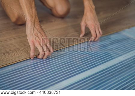 Man Installing New Wooden Laminate Flooring On A Warm Film Floor. Infrared Floor Heating System Unde