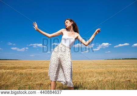 Young beautiful girl in the background of mown wheat field and blue sky