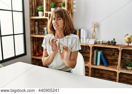 Young caucasian girl wearing casual clothes sitting on the table at home disgusted expression, displeased and fearful doing disgust face because aversion reaction. with hands raised 