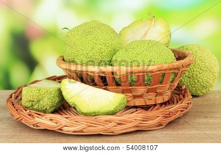 Osage Orange fruits (Maclura pomifera) in basket, on wooden table, on nature background