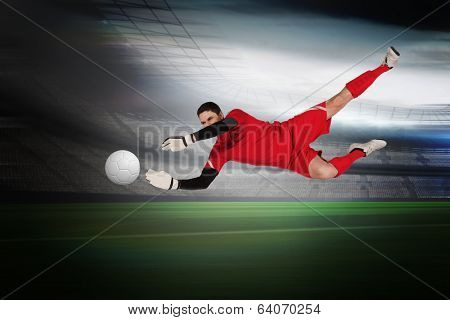 Fit goal keeper jumping up in a large football stadium with lights