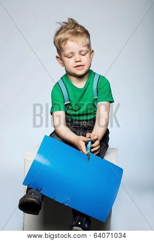 Child boy cutting colored paper with scissors