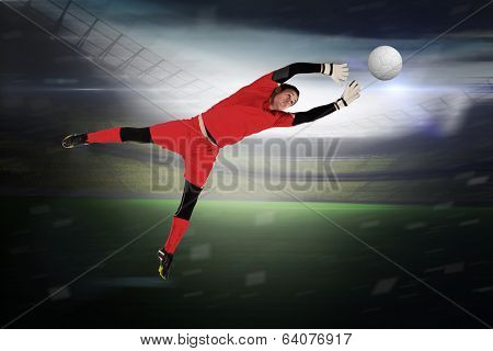 Fit goal keeper jumping up in a large football stadium with lights