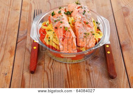 fresh fried natural pink salmon on italian traditional tagliatelle backed with tomato and vegetables served over wooden table with cutlery