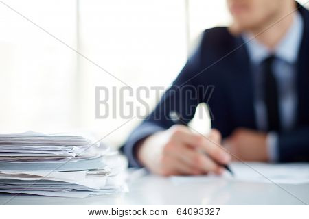 Stack of documents at workplace and male employee on background