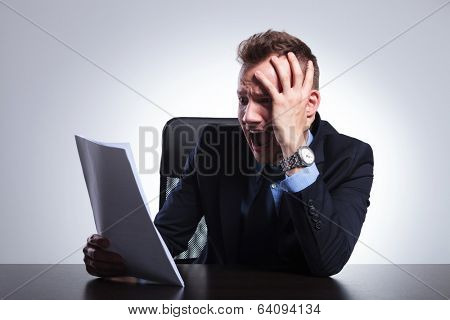 young business man acting scared after reading something on a paper that he is holding. on a light gray studio backgroud