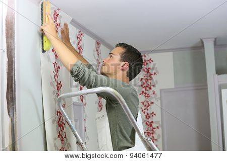 Young apprentice learning how to put wallpaper up on wall