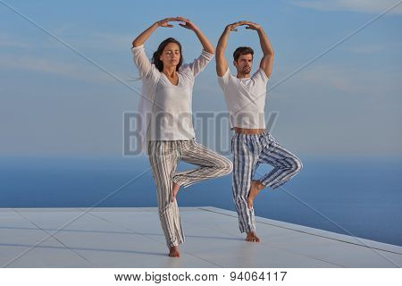 young couple practicing yoga at sunset in modern home terace with ocean and sunset in background